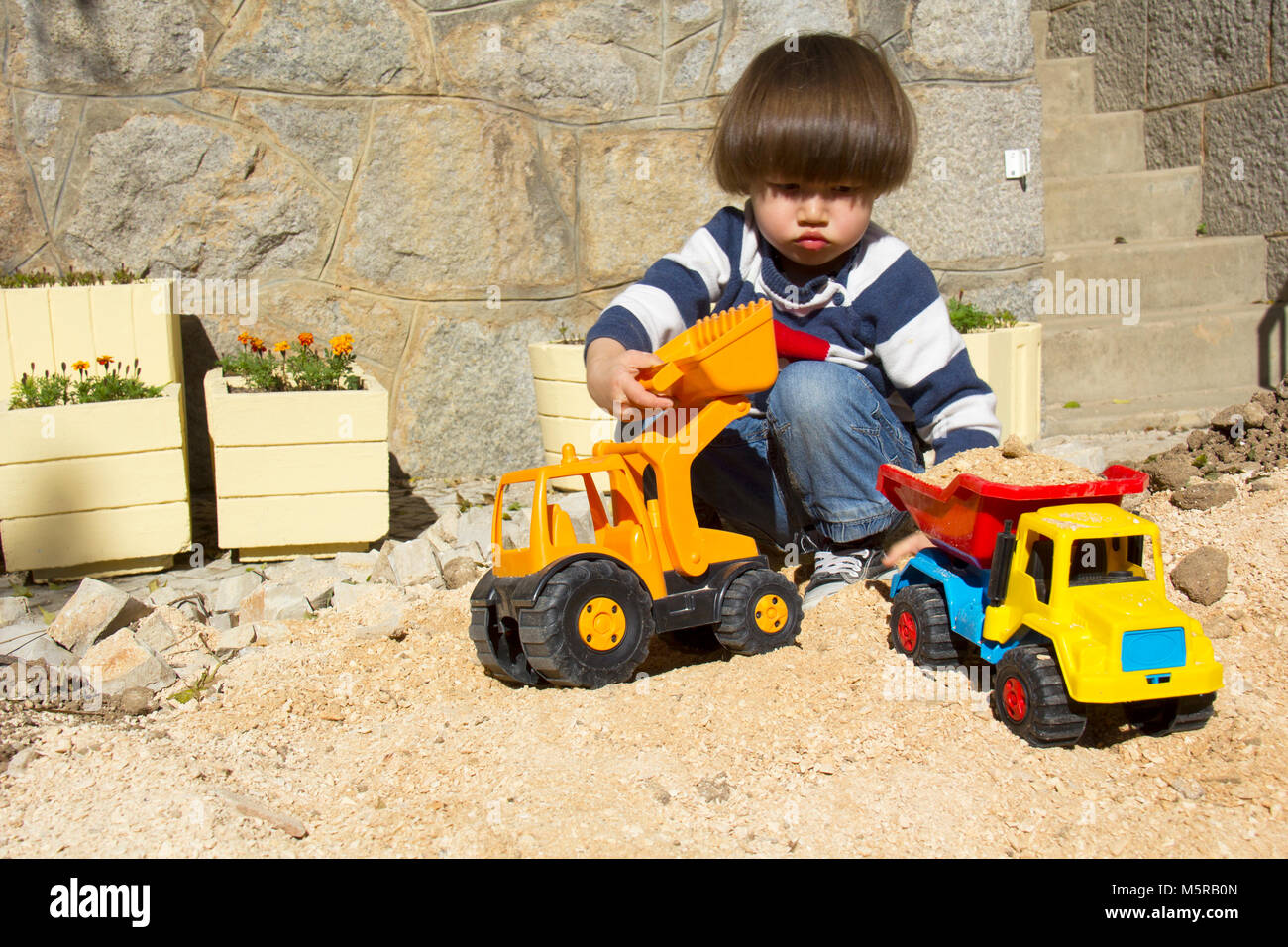 Petit garçon de trois ans jouant dans le sable avec une pelle et camion. Banque D'Images