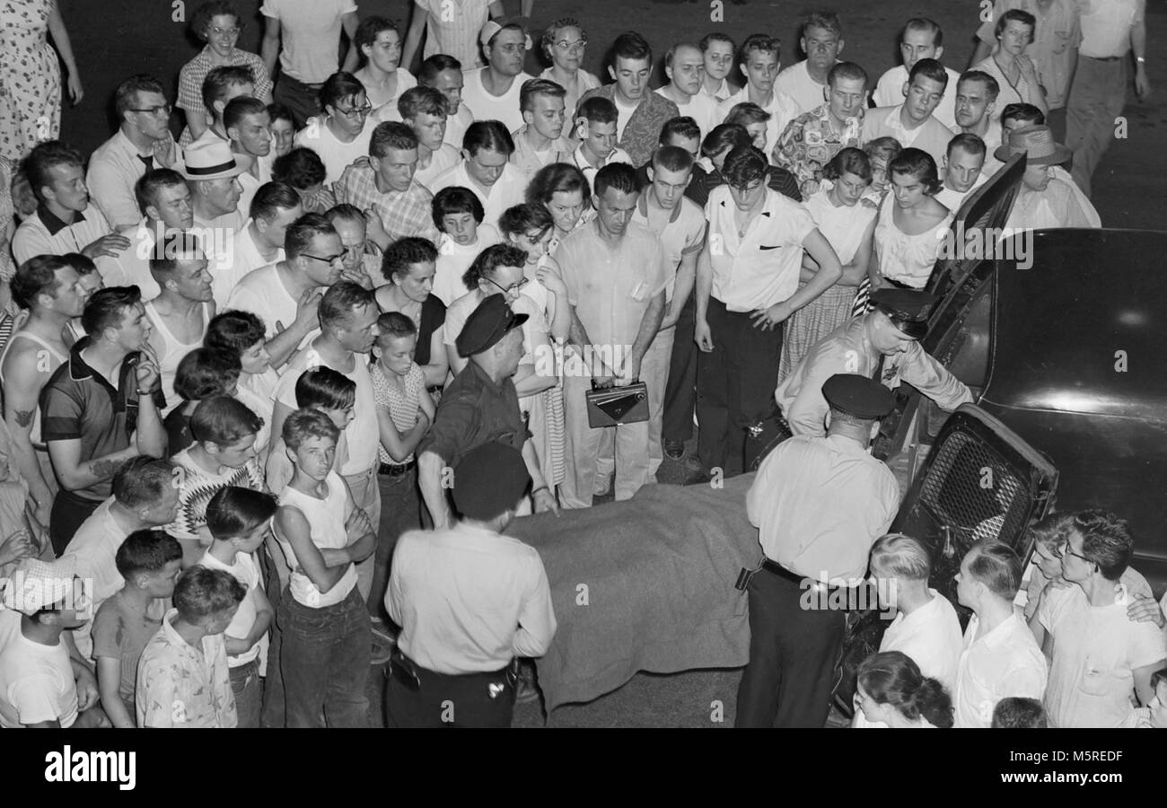 Une foule de quartier comme l'ensemble des montres victime de meurtre est chargé dans le dos de la police hearse dans Chicago, ca. 1955. Banque D'Images