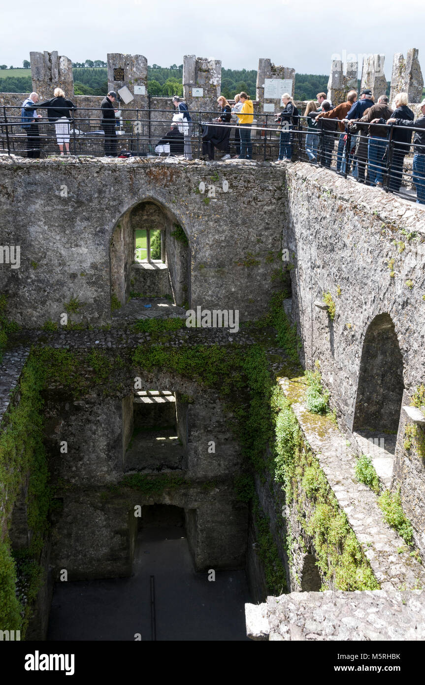 Une longue file de visiteurs regarder une des visiteurs établir avec l'aide d'un membre du personnel du château de la baiser la pierre de Blarney en haut de Banque D'Images