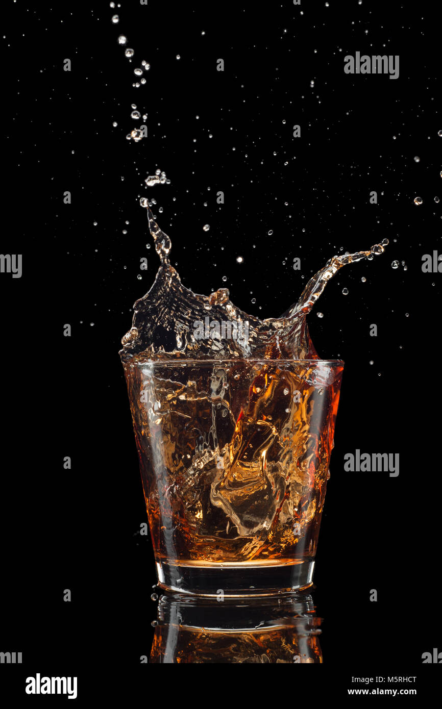 Verre de whisky avec splash isolé sur fond noir. Banque D'Images