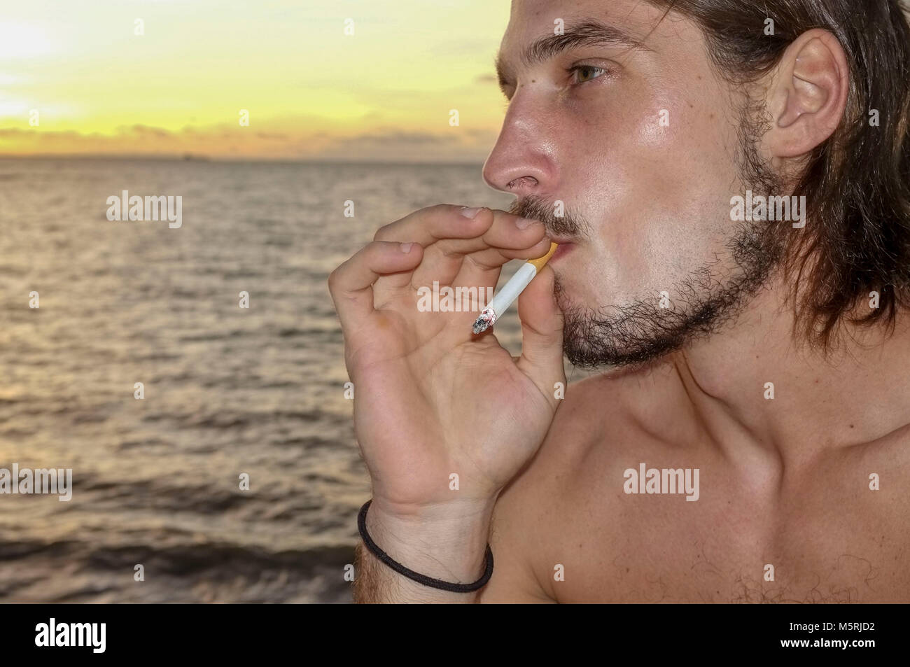 Close-up of a young Caucasian man smoking a cigarette sur la plage. Banque D'Images