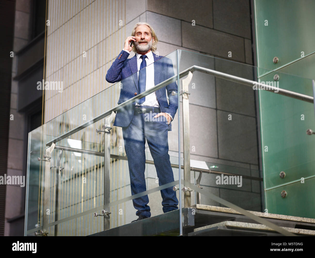 Directeur général de race blanche debout sur haut des escaliers d'effectuer un appel en utilisant votre téléphone mobile en immeuble de bureaux modernes, low angle view. Banque D'Images