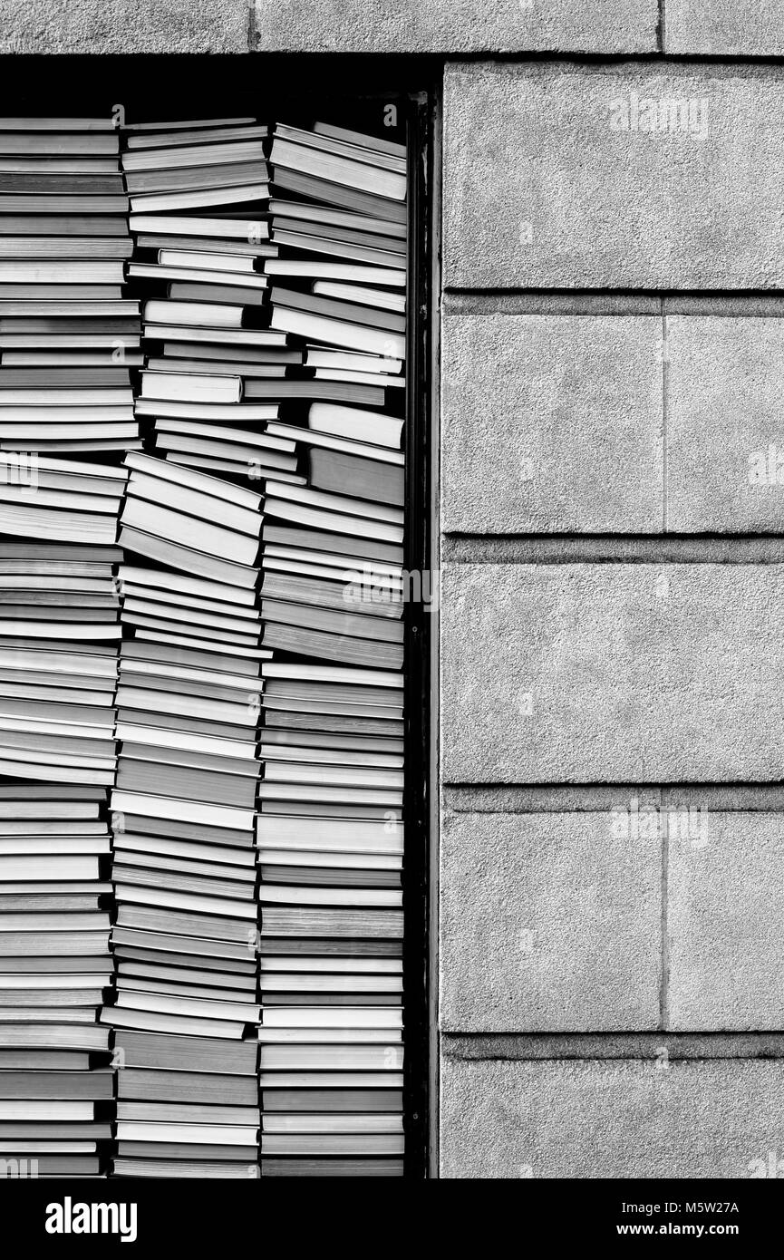 Livres empilés contre fenêtre avec mur de brique à côté d'eux Banque D'Images