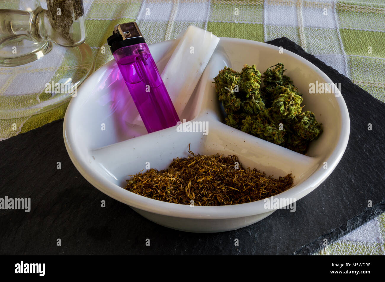 Grand Bong de cristal et la plaque avec des matériaux pour faire un joint et la fumée. Belle Présentation de bourgeons de marijuana, tabac, plus léger et de papier à rouler. Banque D'Images