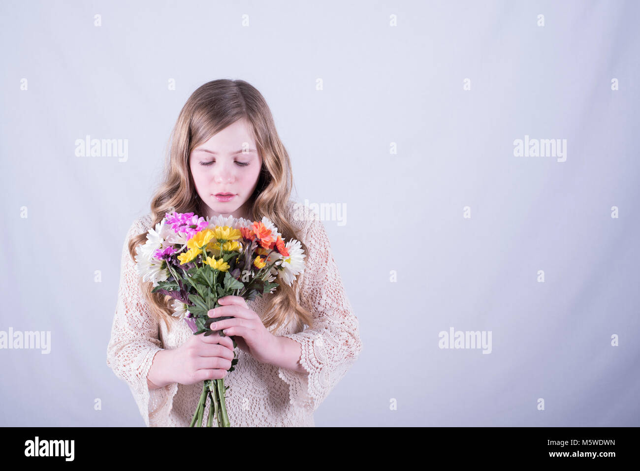 12-year-old fille avec de longs cheveux blond sale, regardant le bouquet de marguerites colorées contre fond blanc Banque D'Images