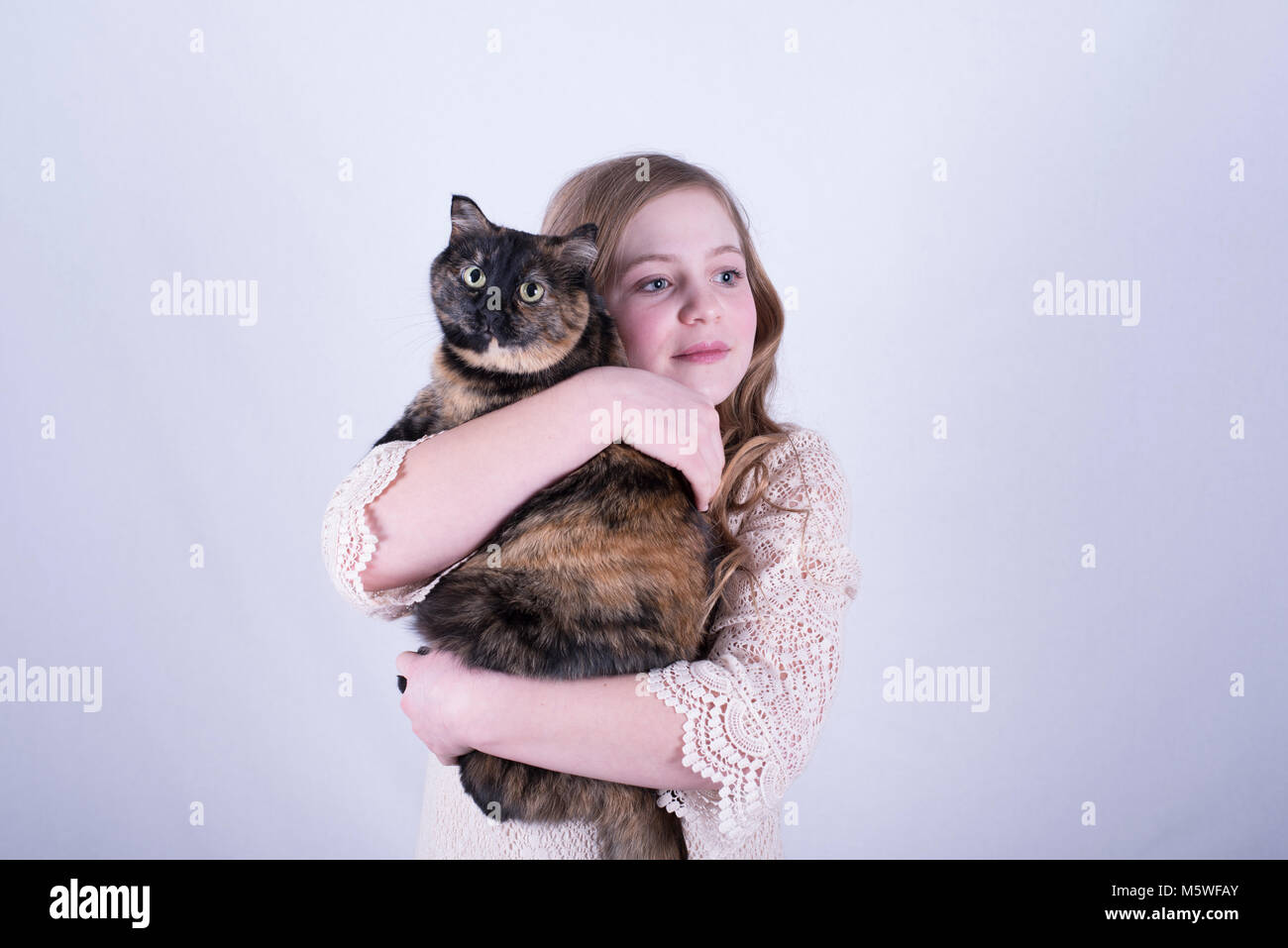 12-year-old fille avec de longs cheveux blond sale, tenant une écaille de chat tout en regardant vers le côté contre fond blanc Banque D'Images