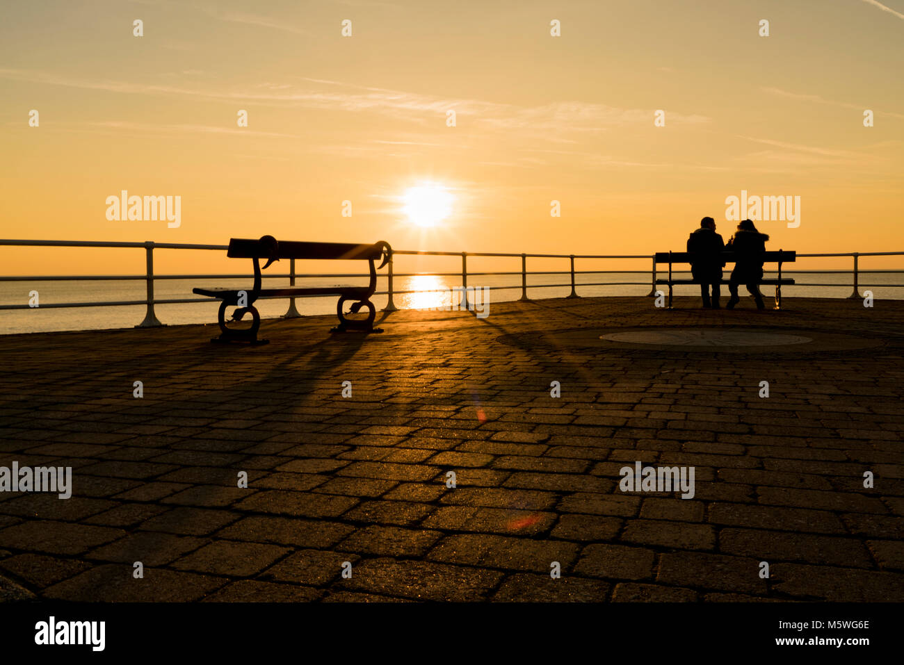 Deux personnes qui se profile par le soleil, regardant notre mer à Aberystwyth, Pays de Galles, Royaume-Uni Banque D'Images