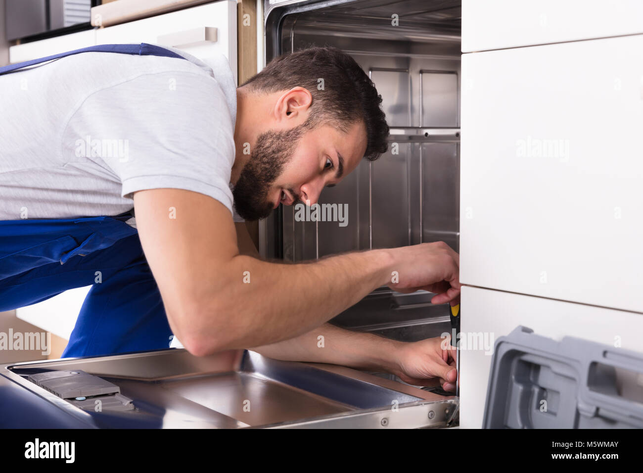 Technicien de jeunes hommes de la réparation d'un lave-vaisselle dans la cuisine Banque D'Images
