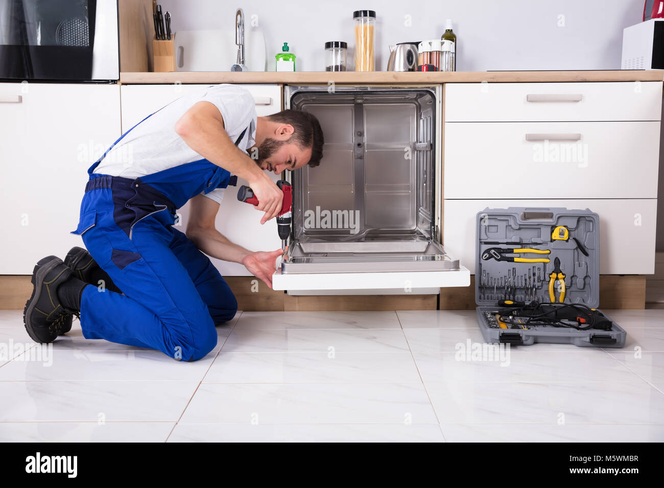 Technicien de jeunes hommes de la réparation d'un lave-vaisselle dans la cuisine Banque D'Images