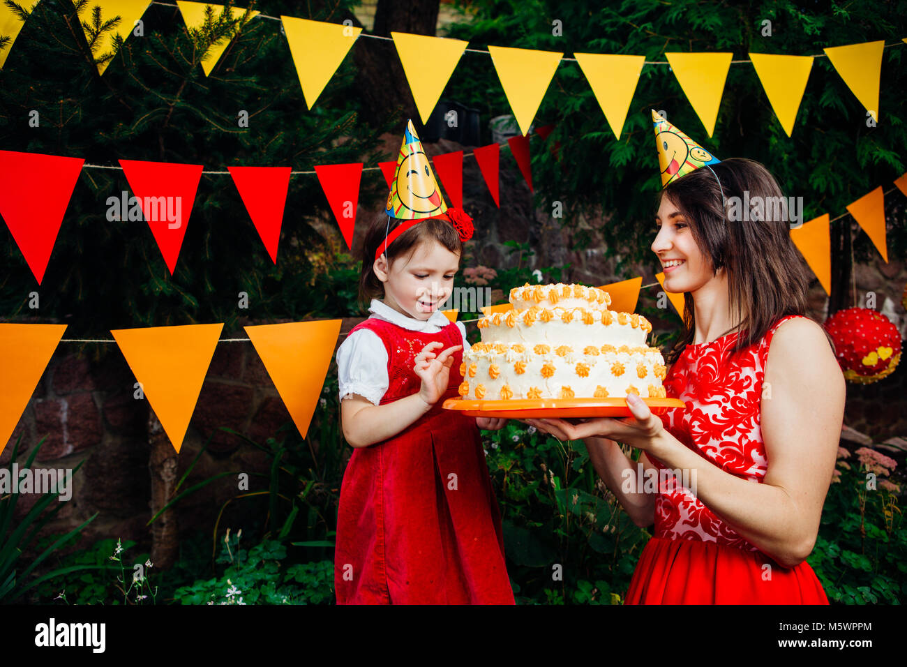 Fete Pour Les Enfants Et Des Gateaux Un Petit Enfant D Un Funny Girl Tente De Fabricants Un Grand Gateau De Deux Etages Pres De Maman Qui Tient Dans Ses Mains Contre L Arriere