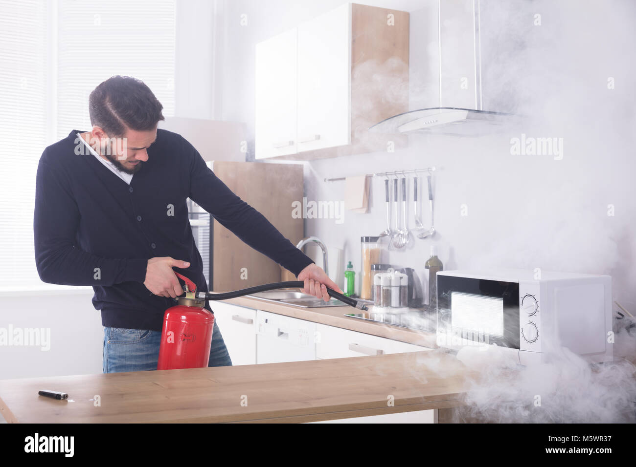 Jeune homme pulvérisant extincteur sur le four à micro-ondes dans la cuisine Banque D'Images