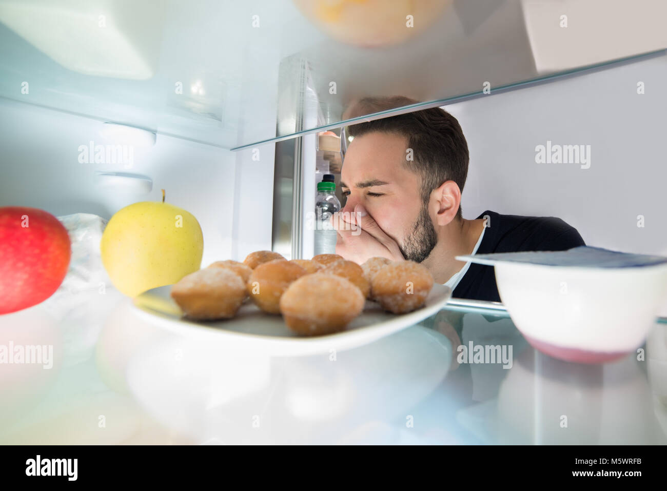 Close-up of a Young Man Holding son nez près de mauvais aliments dans réfrigérateur Banque D'Images