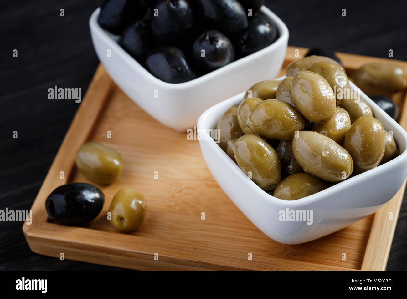 Olives noires et vertes dans un bol blanc sur une table en bois sombre. Banque D'Images