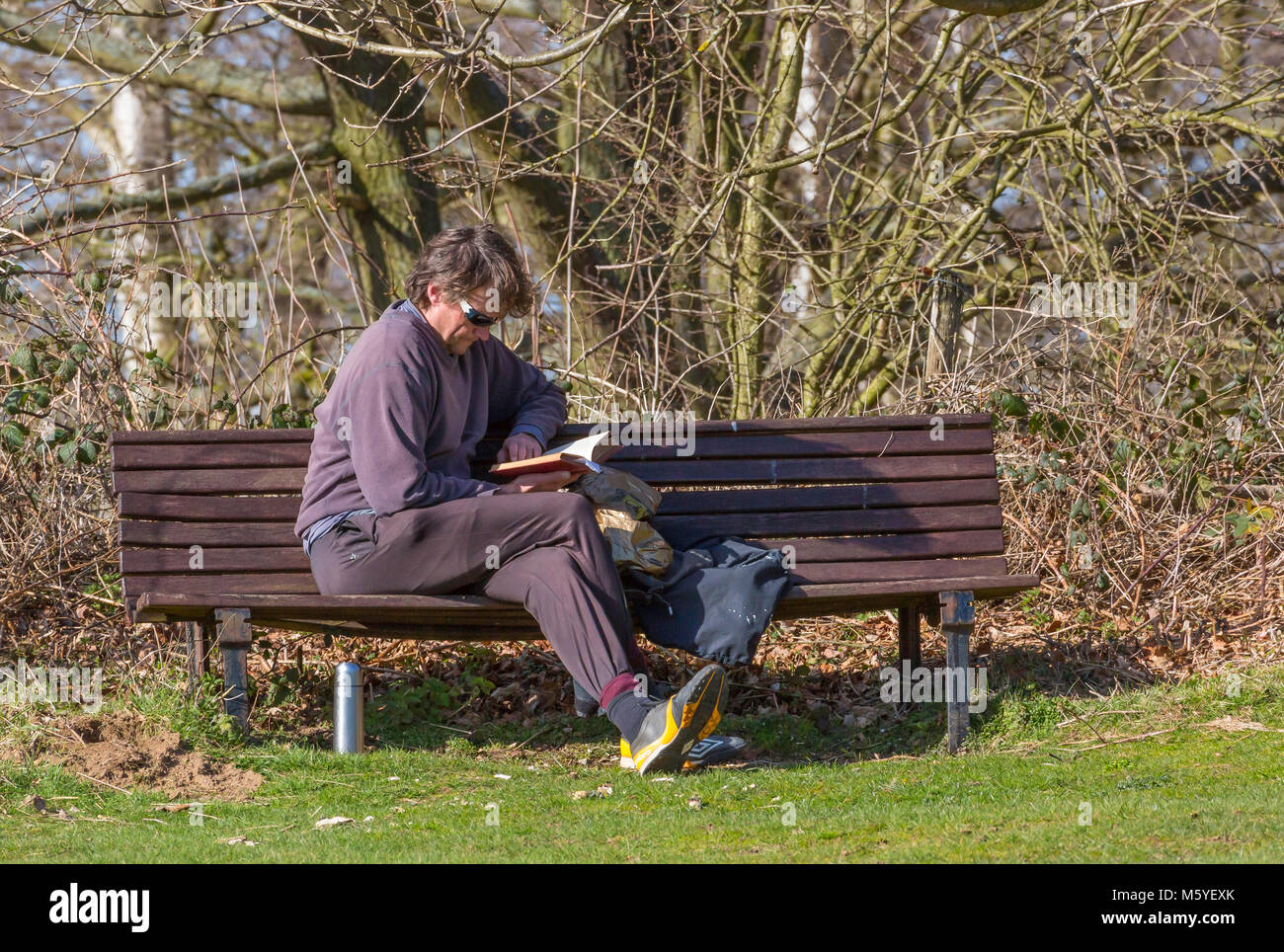 L'homme se détendre sur un banc au soleil avec un livre. Banque D'Images