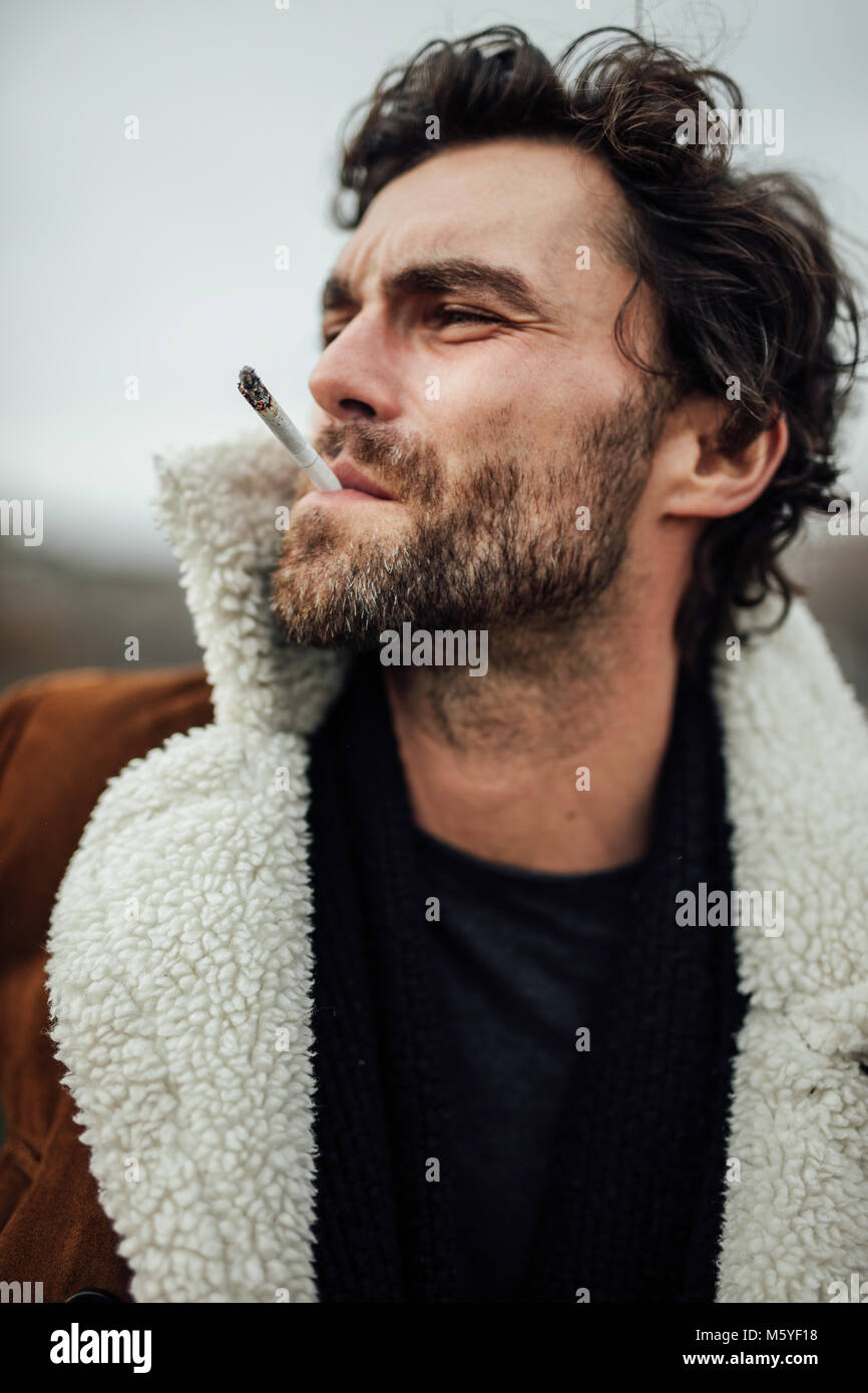Bel homme cool cigarette à l'extérieur dans un manteau d'aviateur avec  l'attente d'une attitude masculine Photo Stock - Alamy