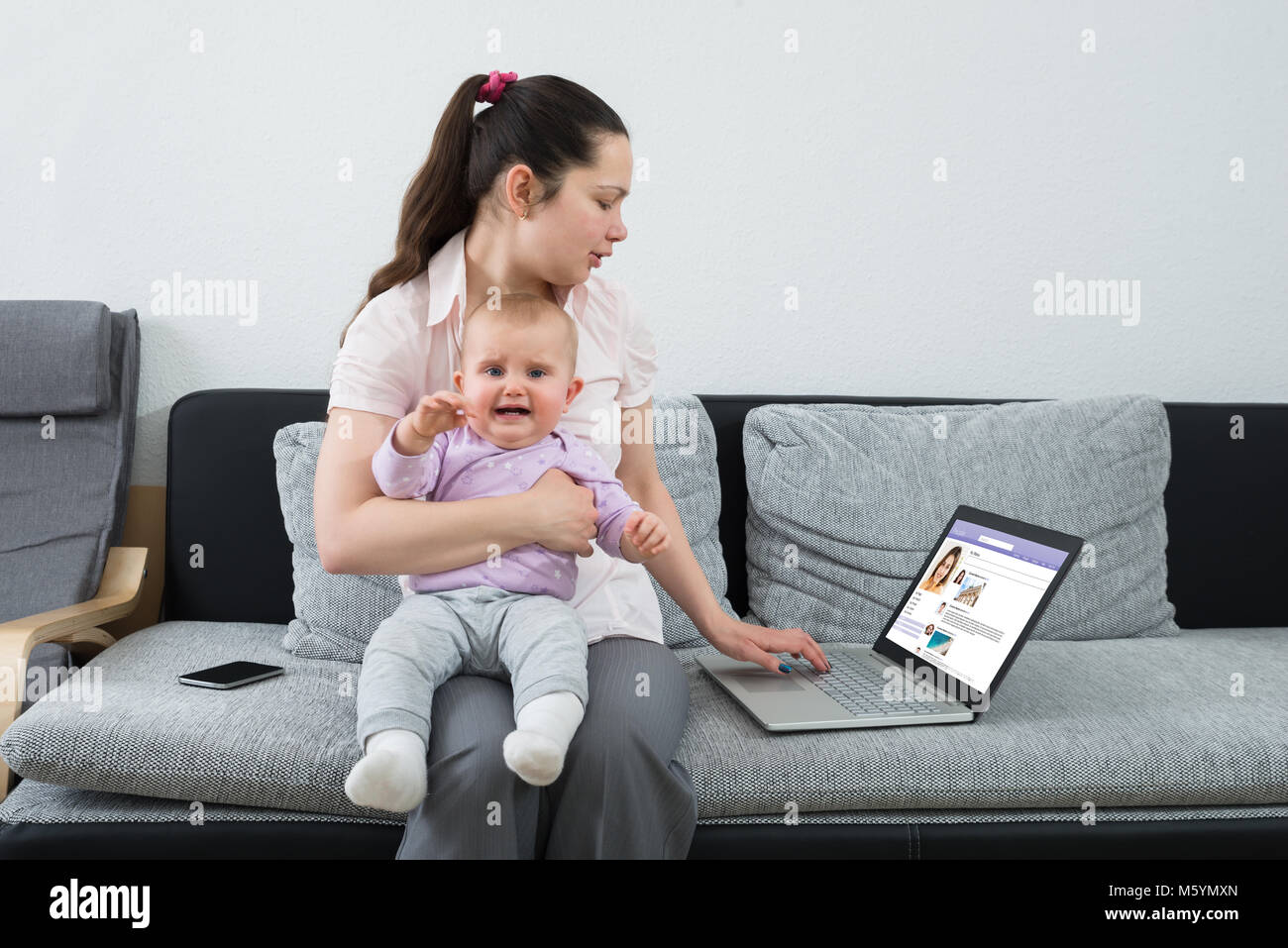 Femme avec son bébé qui pleure sur site de réseautage social Using Laptop Banque D'Images