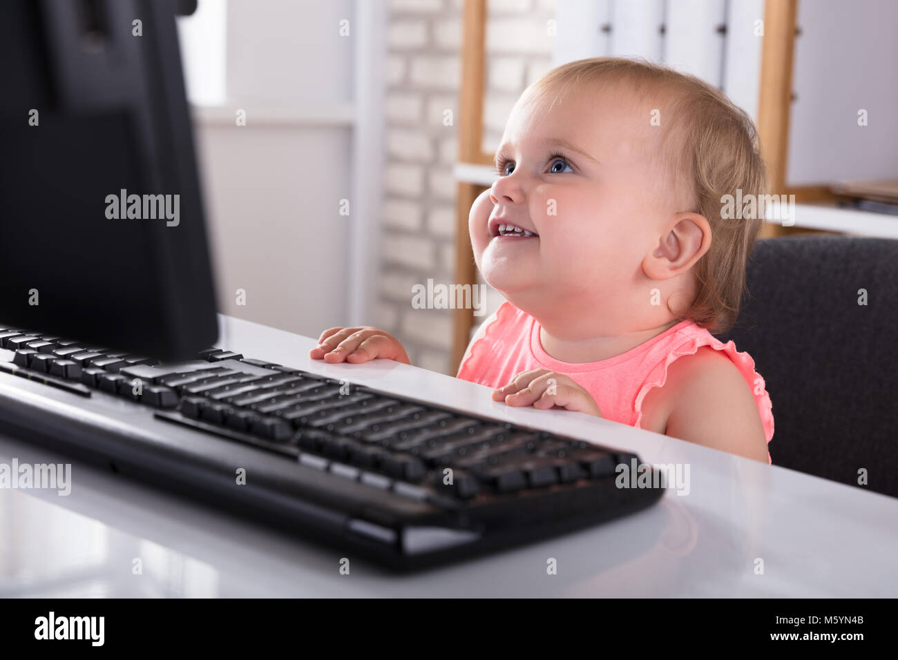 Close-up of Cute Smiling baby girl looking at Computer Banque D'Images