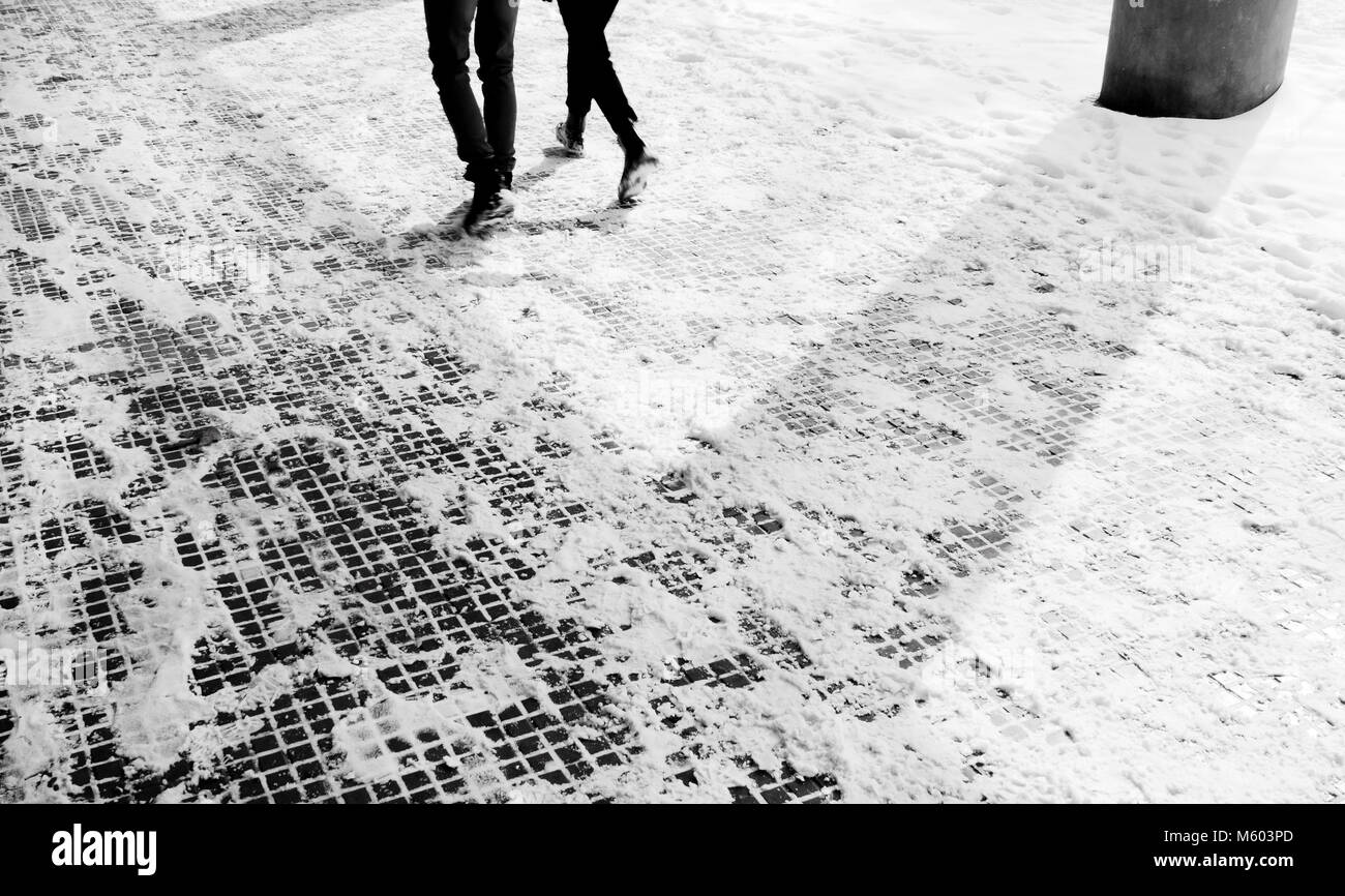 Les jambes de deux personnes marchant sur le trottoir enneigé en mouvement blurin noir et blanc Banque D'Images
