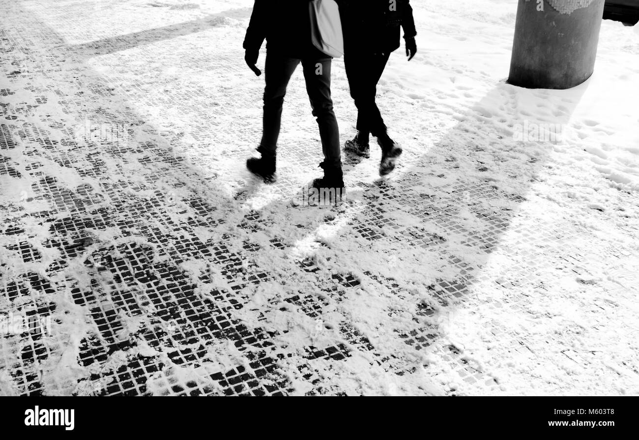 Les jambes de deux personnes marchant sur le trottoir enneigé en mouvement blurin noir et blanc Banque D'Images
