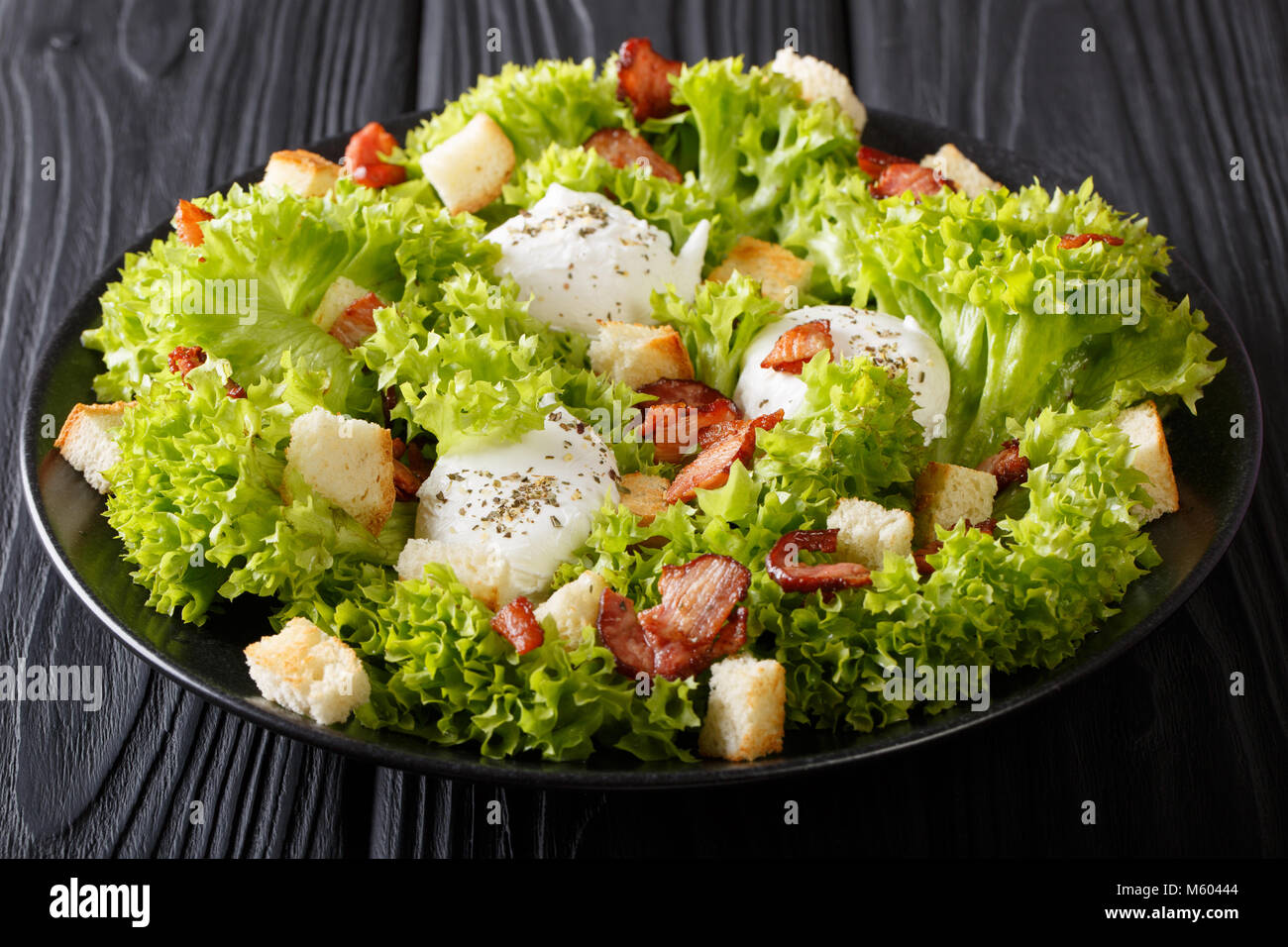 Cuisine française : Salade Lyonnaise de laitue, de bacon, de croûtons et œufs pochés sur une plaque horizontale sur la table. Banque D'Images