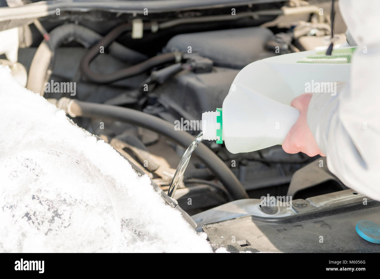 La jeune fille se déverse dans le réservoir d'une voiture sans glace. L'hiver, le jour, le froid. Banque D'Images