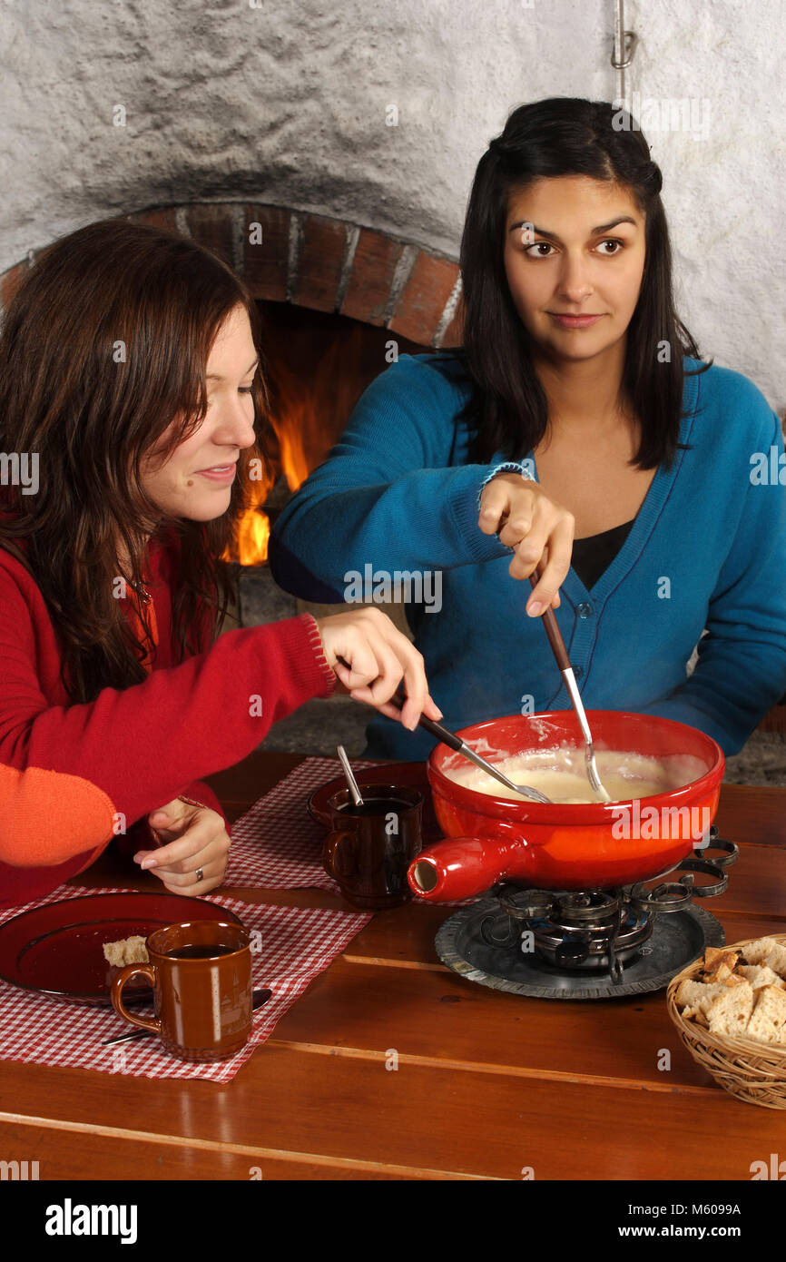 Photo de deux belles femmes trempant dans le pain de fromage fondu dans un caquelon. L'accent est sur la fille de gauche. Banque D'Images