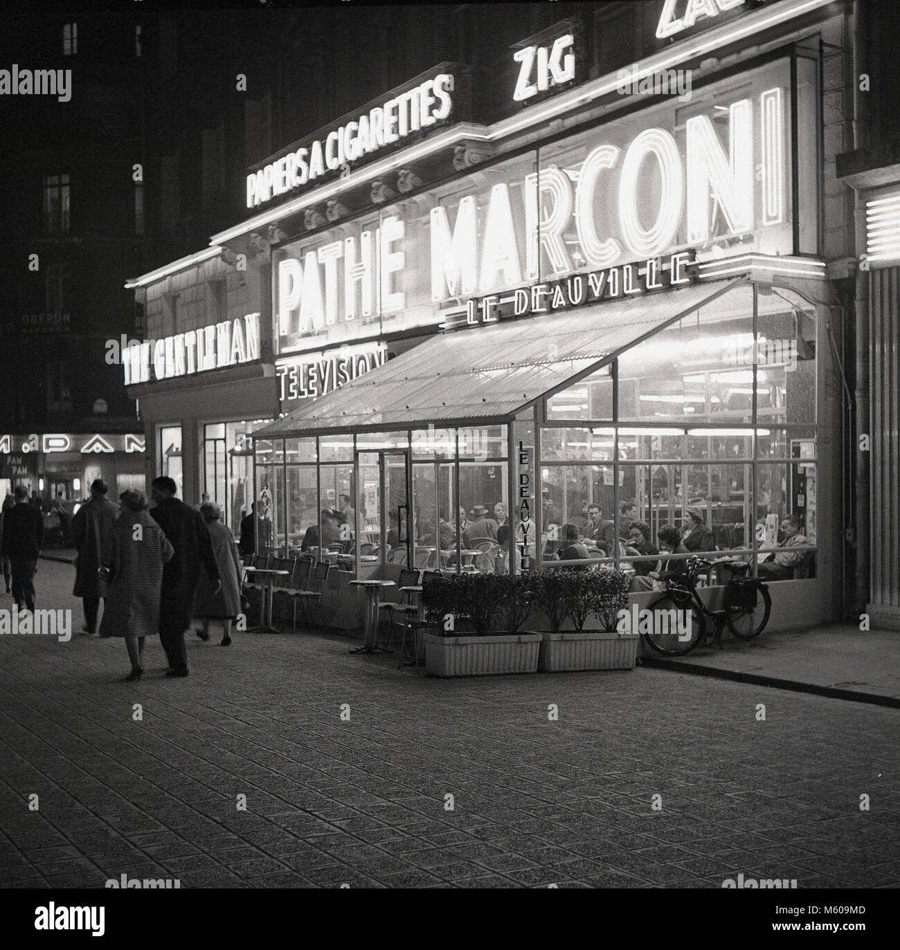 Années 1950, tableau historique de Paris dans la soirée à l'extérieur de cafe Le Deauville, 75 Avenue des Champs Elysées, avec la lumière au néon autour d'elle, montrant les noms des marques de renommée mondiale et Pathe Marconi. Banque D'Images