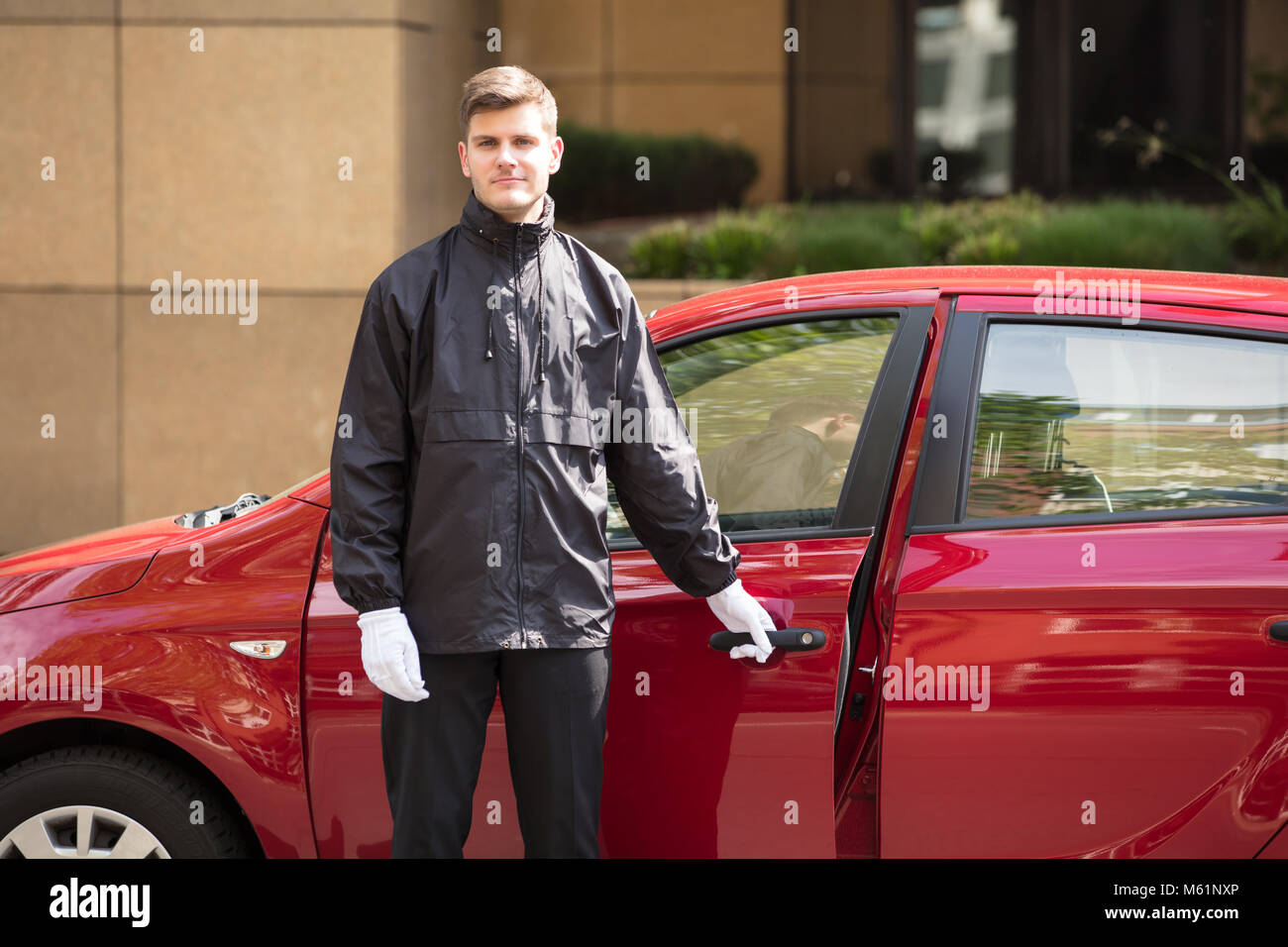 Portrait d'un jeune homme d'ouverture de porte de voiture rouge Valet Banque D'Images
