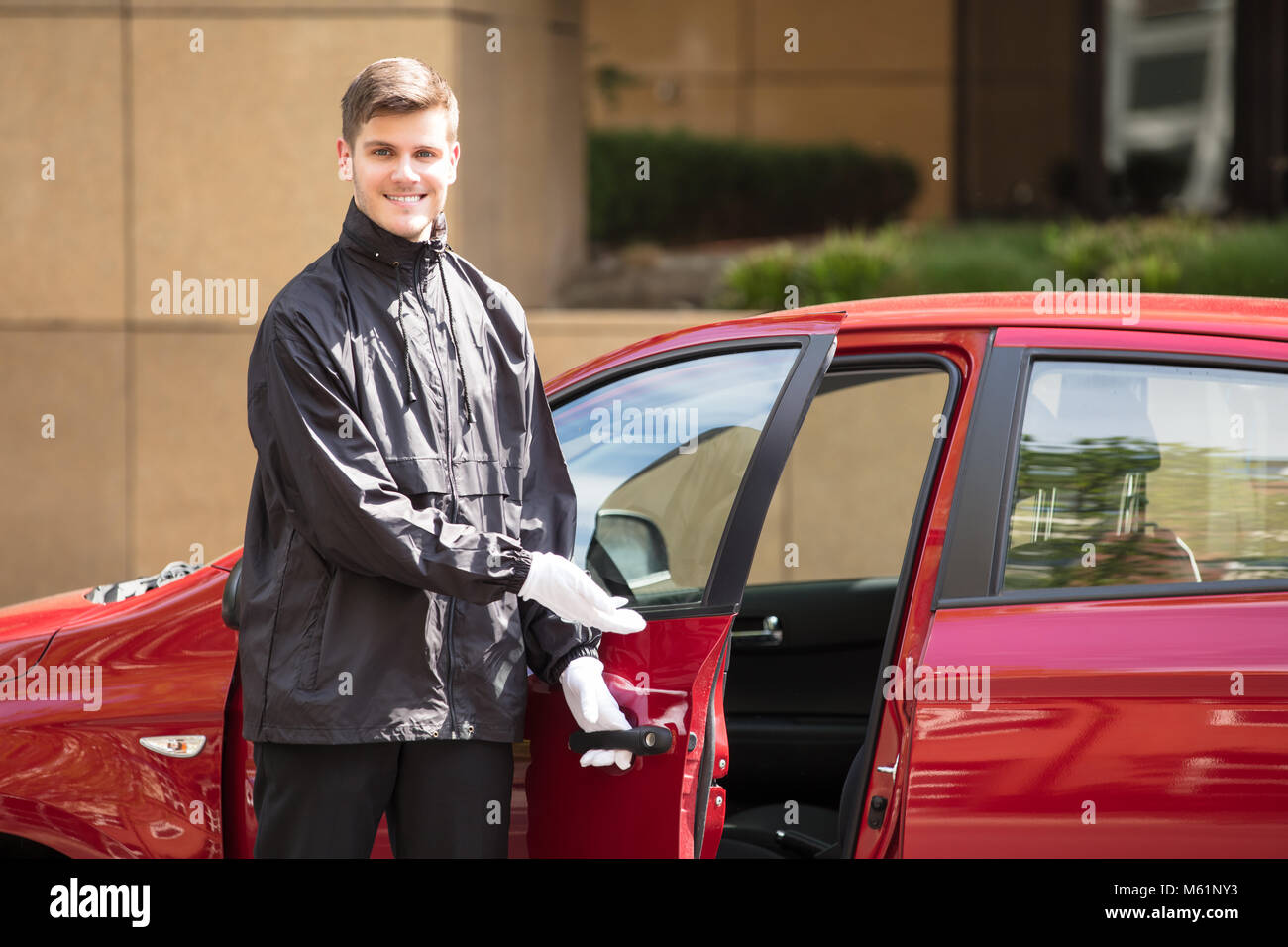 Portrait d'un jeune homme d'ouverture de porte de voiture rouge Valet Banque D'Images