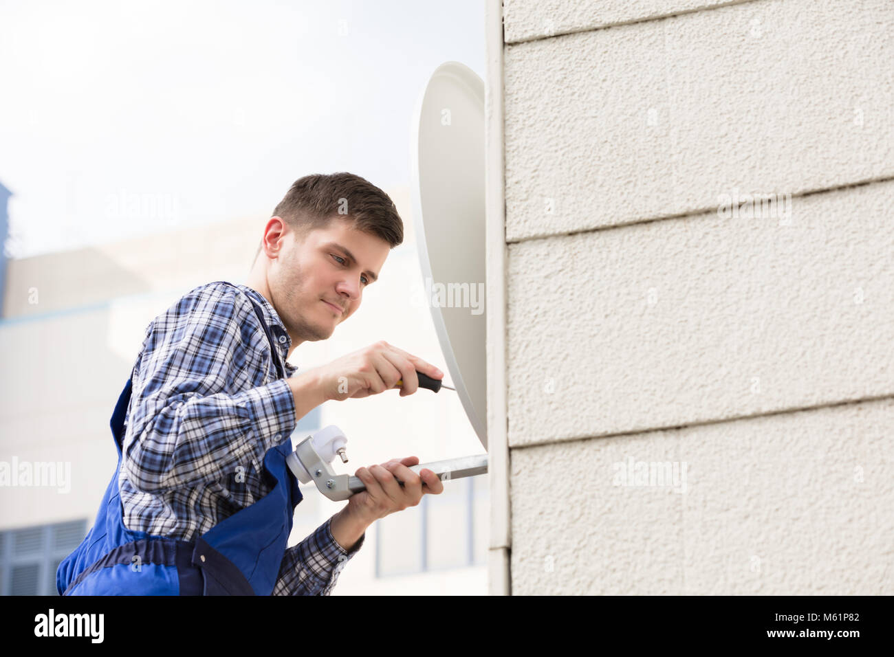 Jeune homme en uniforme pose plat satellite Dish On Wall Banque D'Images
