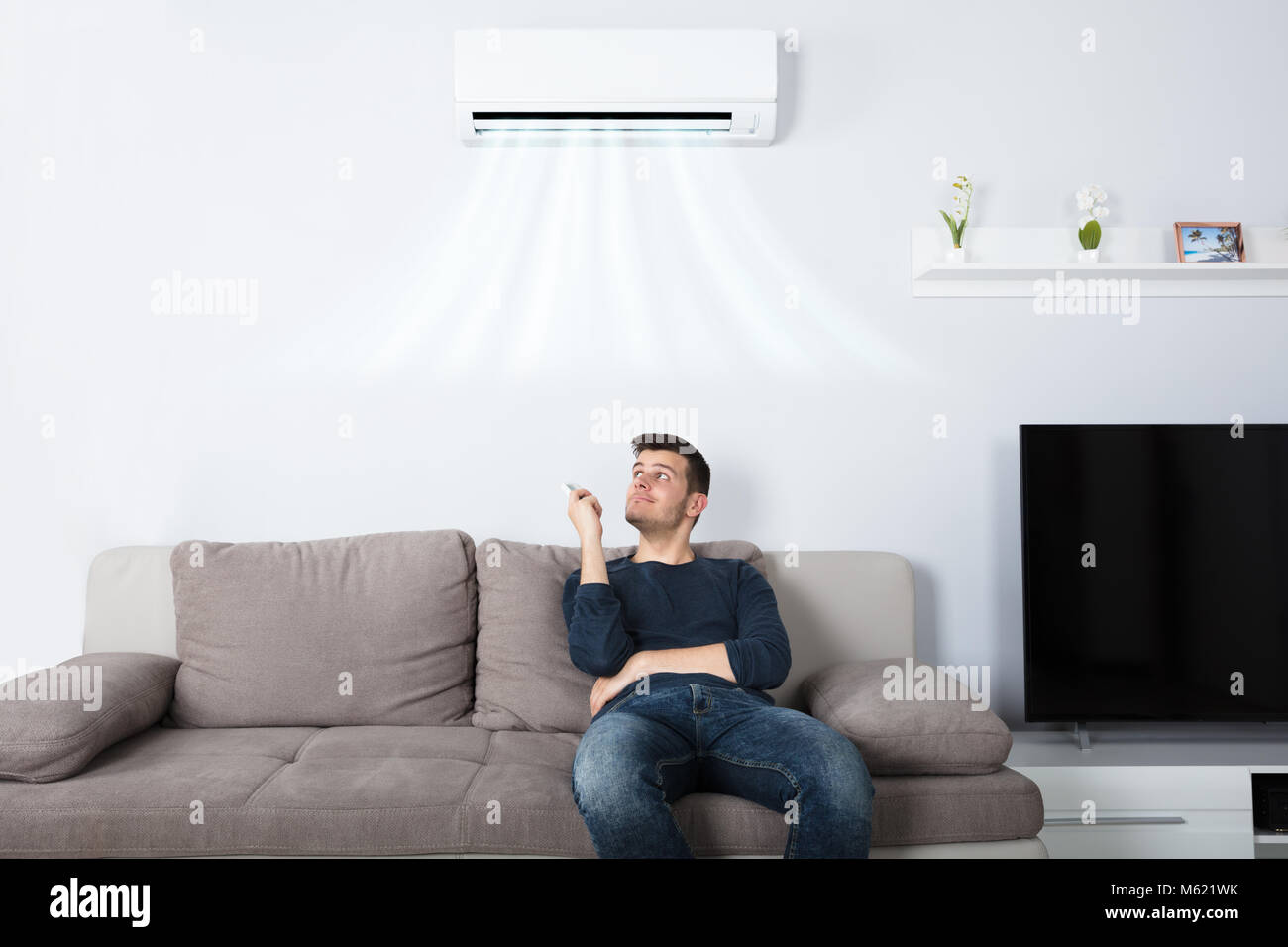 Jeune homme heureux assis sur l'exploitation de la table Air conditionné avec télécommande à la maison Banque D'Images