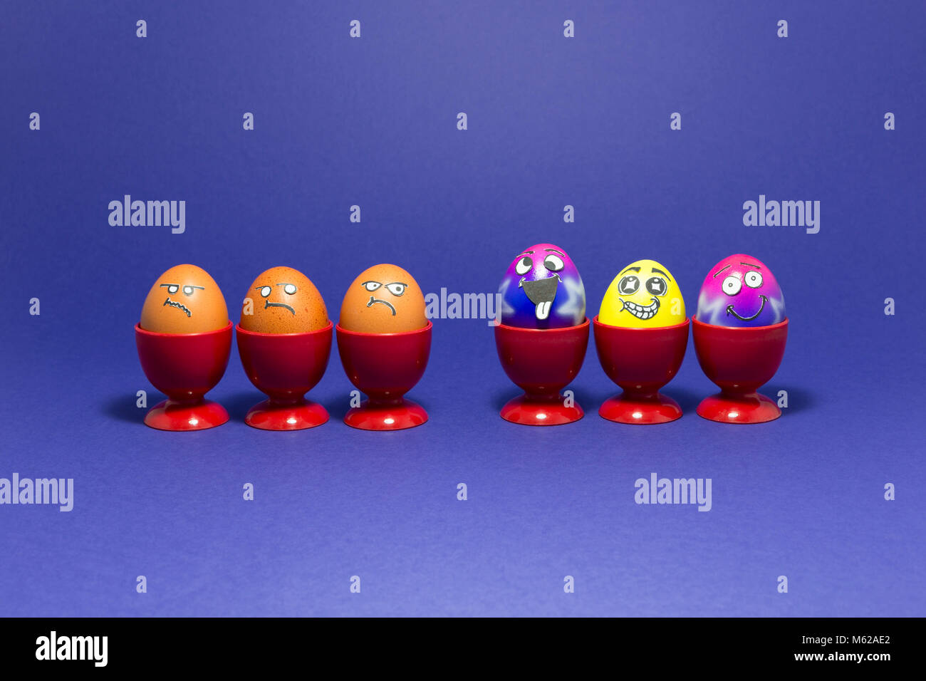 Groupe d'oeufs de Pâques peints colorés avec funny cartoon visages de style et de groupe de grincheux à oeufs brun rouge à l'œuf en plastique tasses sur purple backgrou Banque D'Images