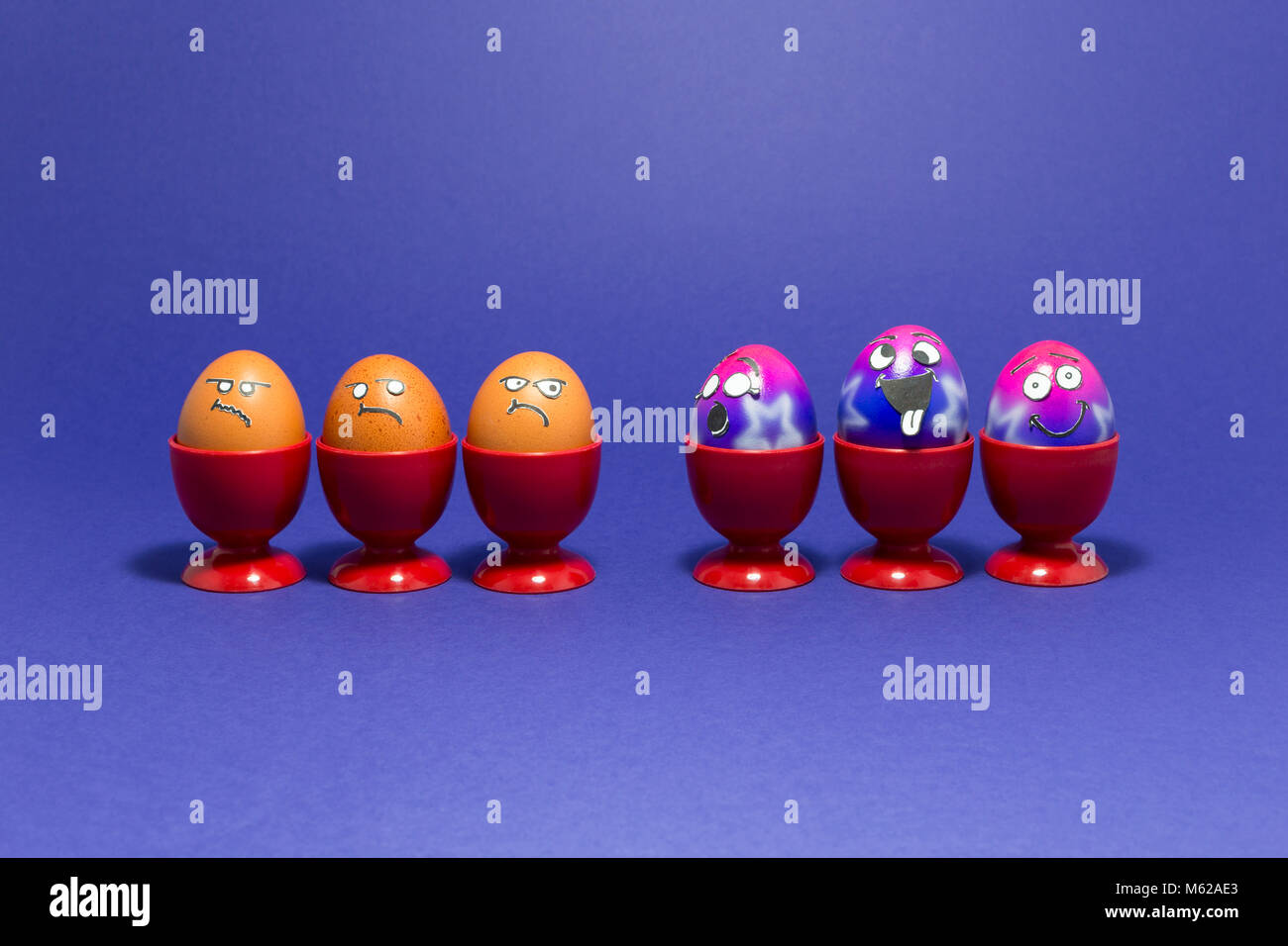 Groupe d'oeufs de Pâques peints colorés avec funny cartoon visages de style et de groupe de grincheux à oeufs brun rouge à l'œuf en plastique tasses sur purple backgrou Banque D'Images
