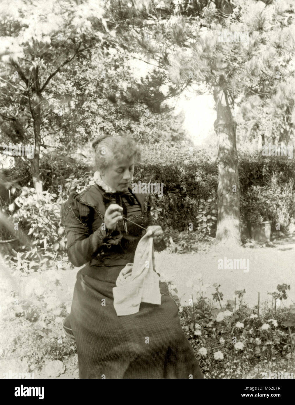 Couture femme victorienne dans son jardin avec lumière pommelé - dans une ferme près de Gloucester, Gloucestershire, Angleterre c. 1900 Banque D'Images