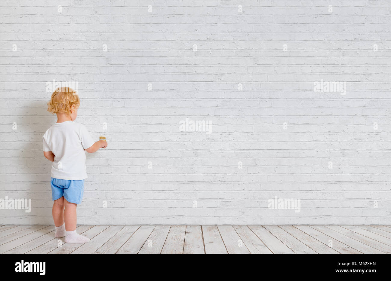 Baby Boy avec le pinceau debout dos près de brick wall Banque D'Images