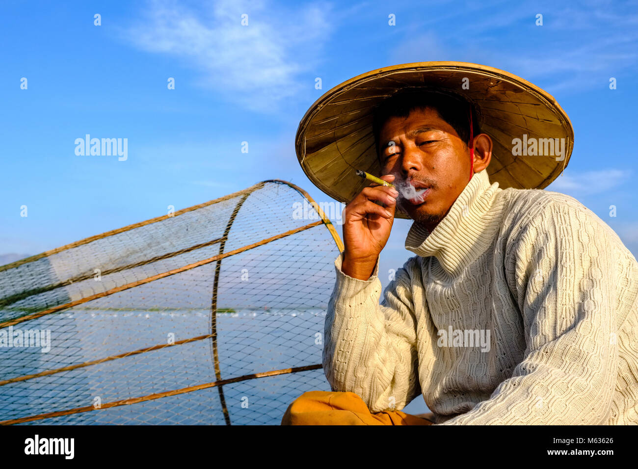 Portrait d'un pêcheur, assis sur son bateau de pêche, de fumer la façon traditionnelle sur le lac Inle Banque D'Images