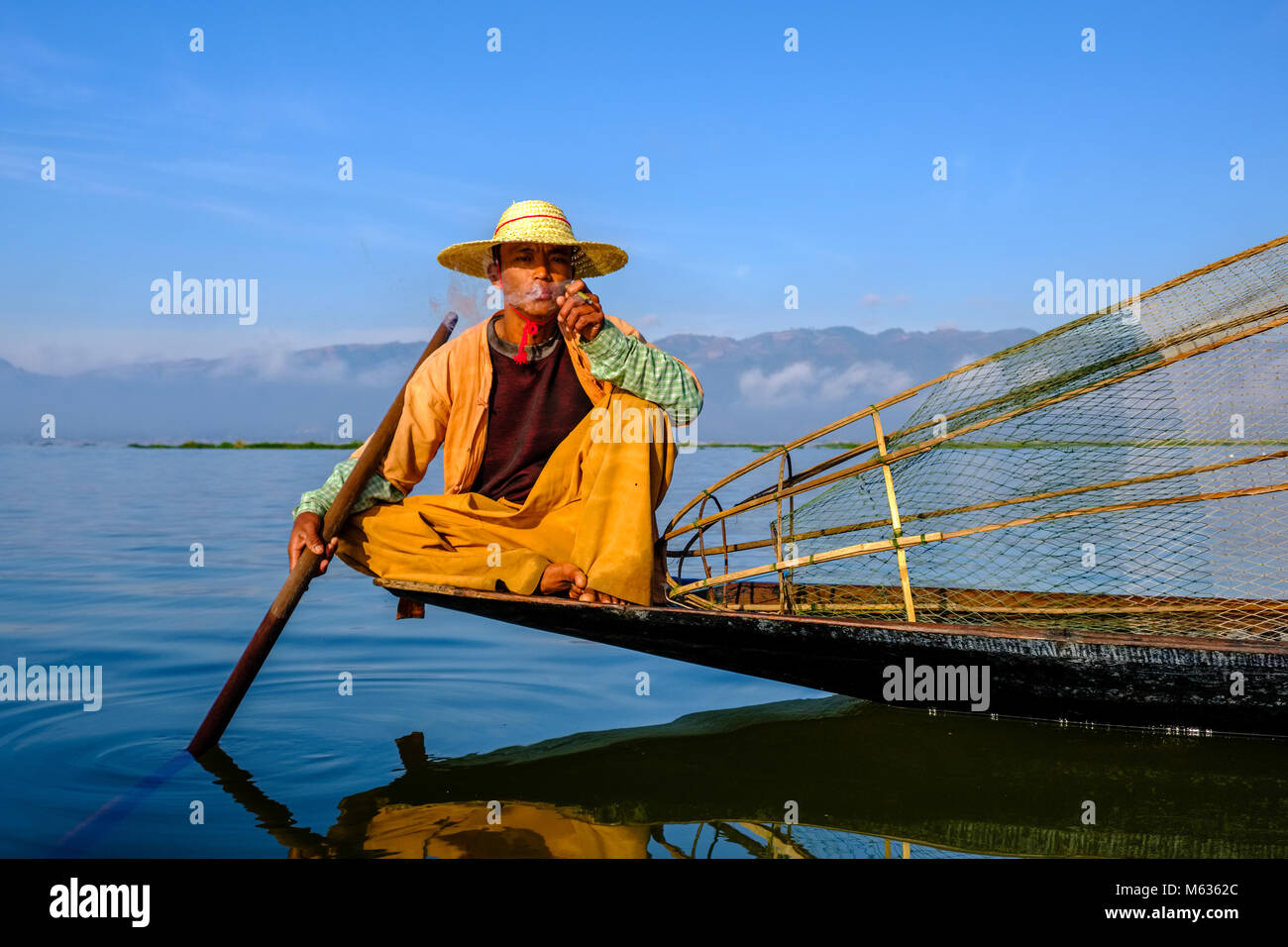 Un pêcheur, assis sur son bateau, le tabagisme est la façon traditionnelle de pêche sur le lac Inle Banque D'Images