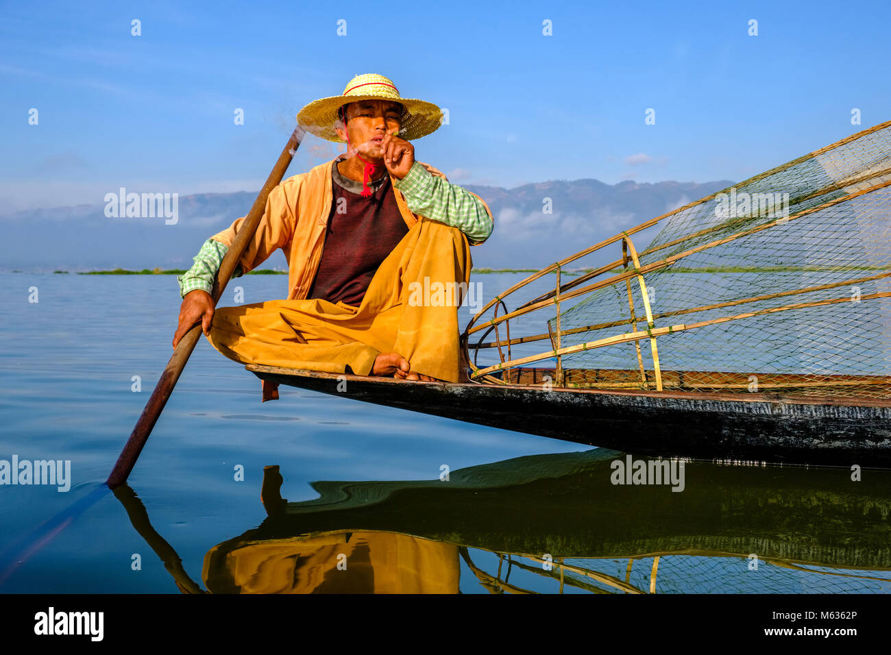 Un pêcheur, assis sur son bateau, le tabagisme est la façon traditionnelle de pêche sur le lac Inle Banque D'Images