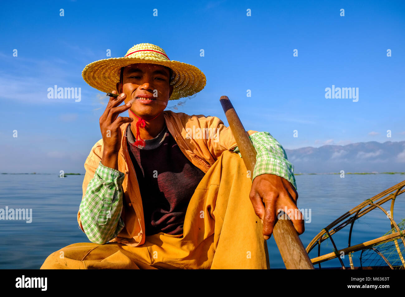 Portrait d'un pêcheur, assis sur son bateau de pêche, de fumer la façon traditionnelle sur le lac Inle Banque D'Images