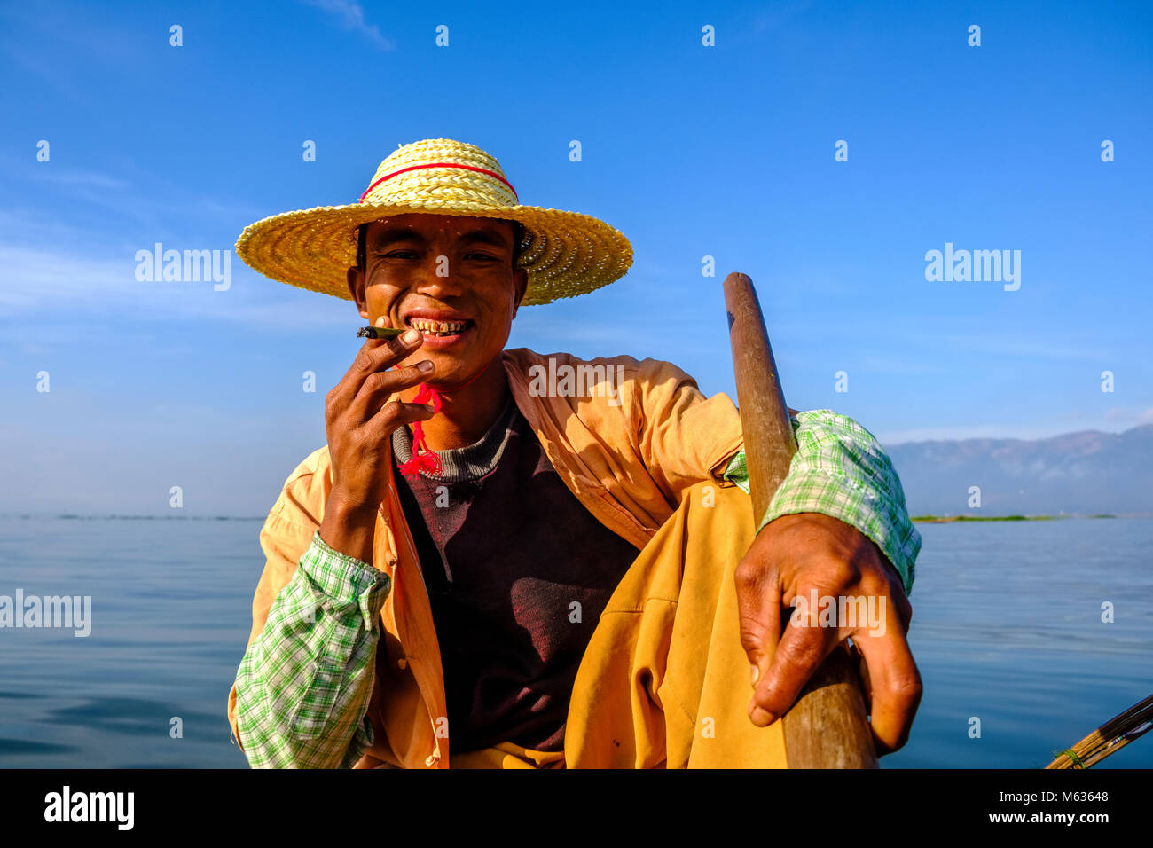 Portrait d'un pêcheur, assis sur son bateau de pêche, de fumer la façon traditionnelle sur le lac Inle Banque D'Images