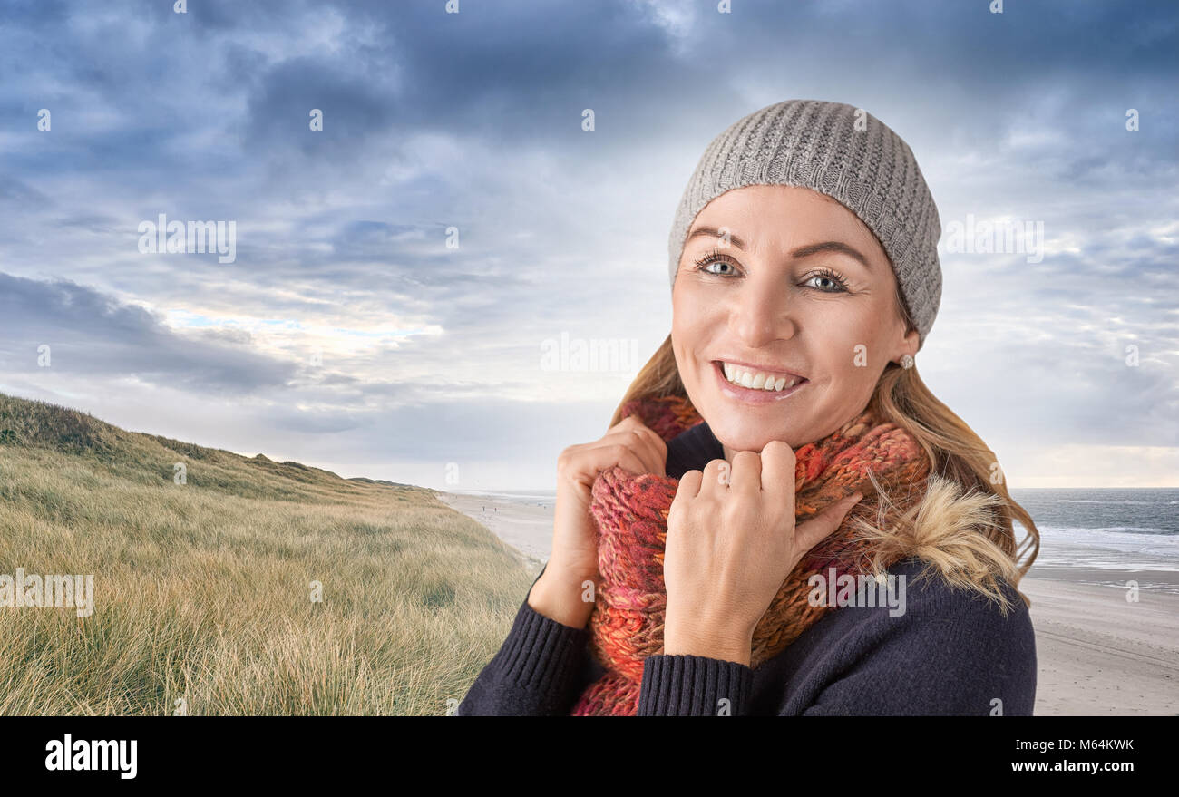 Belle femme d'âge moyen portant un chapeau tricoté et l'écharpe de laine rouge coloré a tenu jusqu'à son cou l'article smiling joyeusement à la surenchère de l'appareil photo Banque D'Images