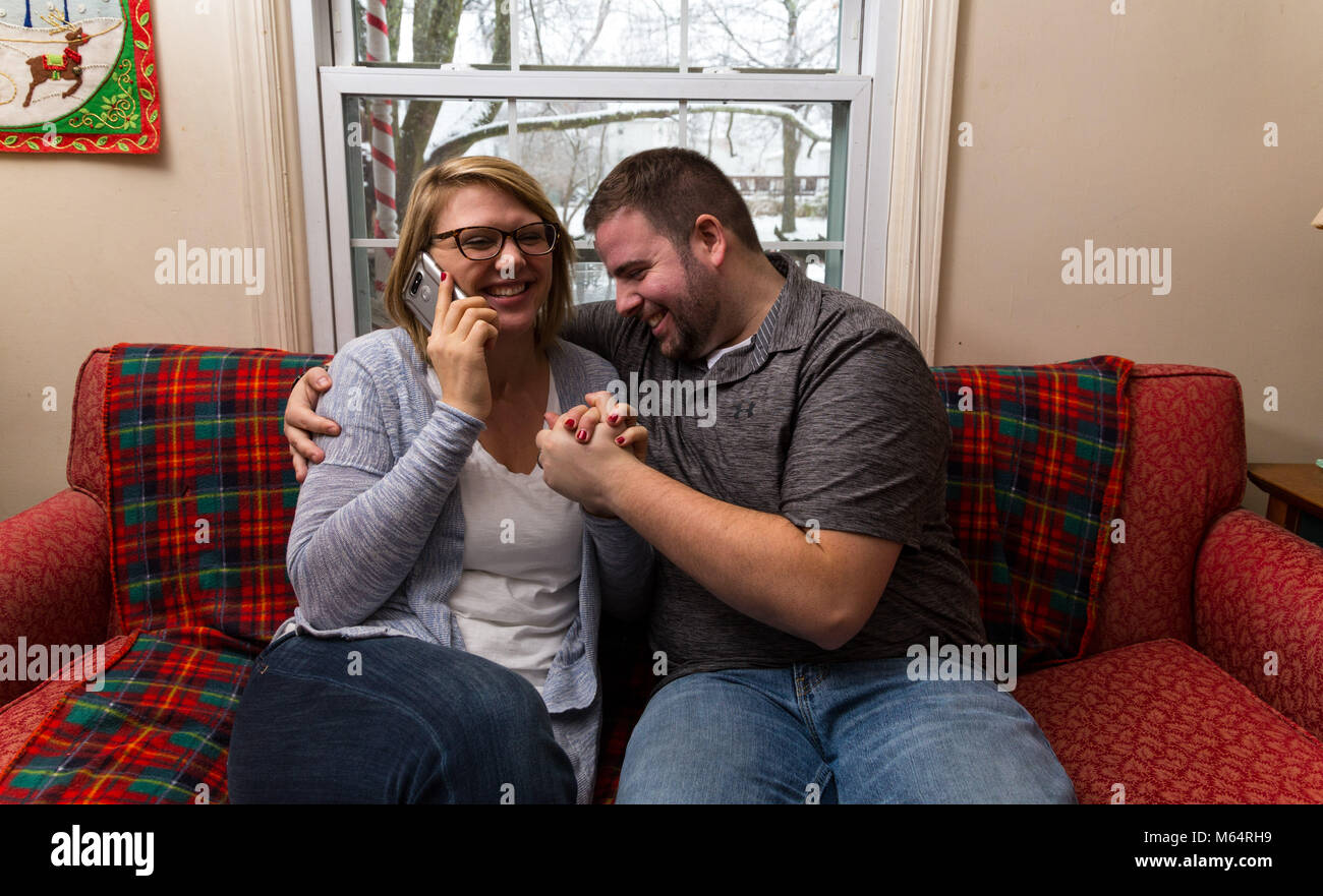 Un jeune couple attend avec enthousiasme et prie pour une bonne nouvelle, car ils sont assis sur leur canapé du salon. Banque D'Images