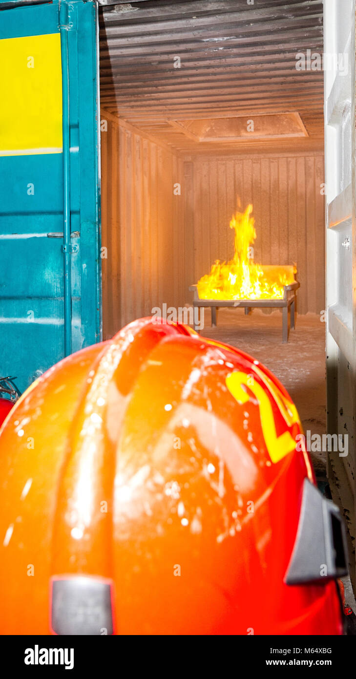 Fireman durant la formation. Extincteur. Flammes jaune doré / incendie dans l'arrière-plan. Casque rouge. Banque D'Images