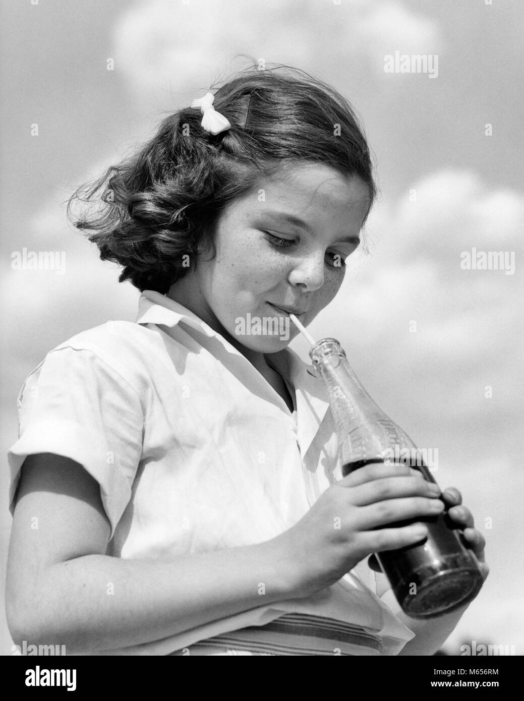 1950 fille brune LA CONSOMMATION DE BOISSONS SODA BOISSON SOFT DRINK À PARTIR DE BOUTEILLE EN VERRE AVEC UNE PAILLE - f4037 HAR001 JOYEUX JOYEUX SOURIRES HARS BOISSON SOFT DRINK MINEURS PRÉ-ADO fille préadolescente B&W NOIR ET BLANC BARRETTE ETHNICITÉ CAUCASIEN GAZEUSES Old Fashioned Banque D'Images
