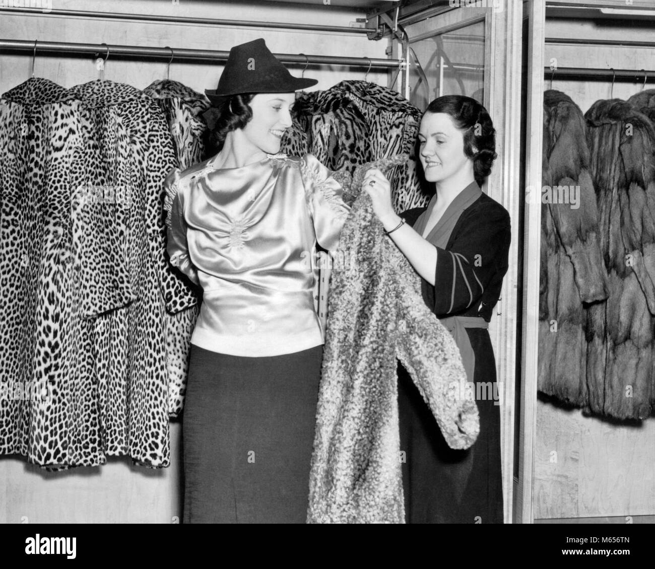 1930 SMILING WOMAN IN FUR BEAUTÉ ESSAYANT SUR LEOPARD manteau, avec l'aide de vendeuse - f8342 HAR001 HARS LEOPARD DEUX PERSONNES RICHES CAUCASIAN WORKMAN RICHE HEUREUX JOIE VIE FEMELLES VENDEUR AU DÉTAIL DE LUXE EMPLOI GROWNUP MANTEAUX pleine longueur MESDAMES INSPIRATION des animaux à l'intérieur nostalgie de 20 à 25 ans Personnes Histoire de l'OCCUPATION DES OUVRIERS VENTE BONHEUR GAI STYLES DE LOISIRS SERVICE CLIENT CHOIX DE LA MAIN-D'EXCITATION D'ESSAYER DE LES JOYEUX SOURIRES FIERTÉ FASHIONS PEAUX peaux de léopards en peau de léopard MARCHANDS VENDEUSE VENDEUR ESSAYANT D'AIDER LES JEUNES ADULTES marchand de fourrures FEMME B&W Banque D'Images