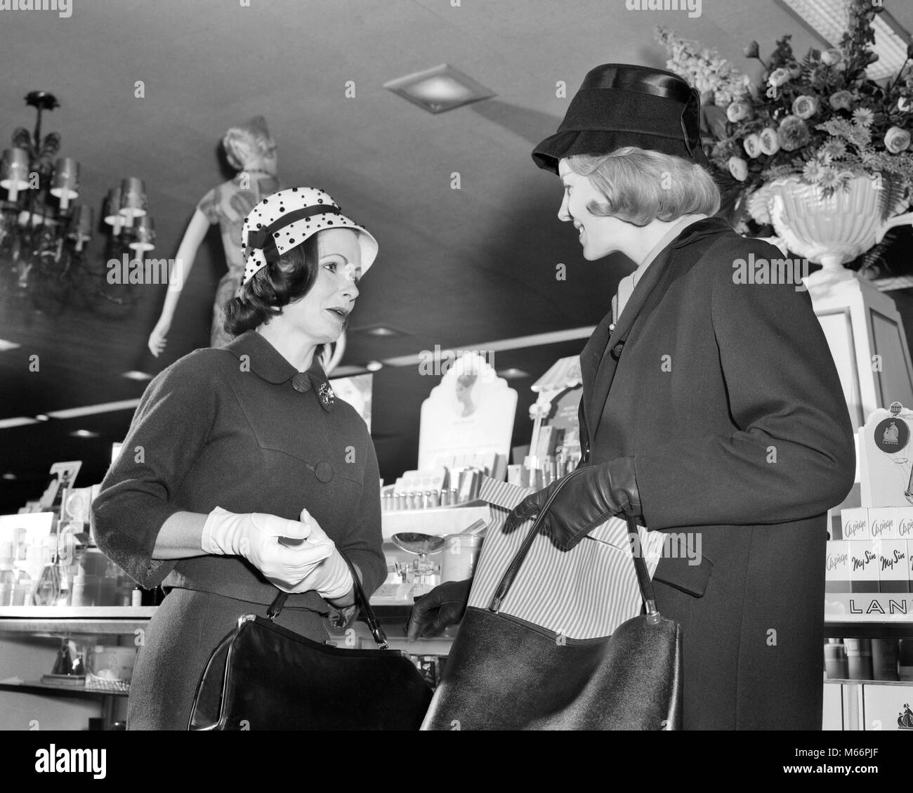 1960 Deux femmes portant des chapeaux en parlant de réunion DEBOUT EN FACE DE COMPTOIR COSMÉTIQUE DE STORE - s14038 HAR001 HARS 25-30 ans 30-35 ans ENSEMBLE STYLES SHOPPERS LOW ANGLE ESTHÉTIQUE MODE CONNEXION GANTS BLANCS MID-ADULT WOMAN FEMME B&W NOIR ET BLANC PORTRAIT DE L'ORIGINE ETHNIQUE DES PERSONNES À L'ANCIENNE DES GANTS EN CUIR Banque D'Images