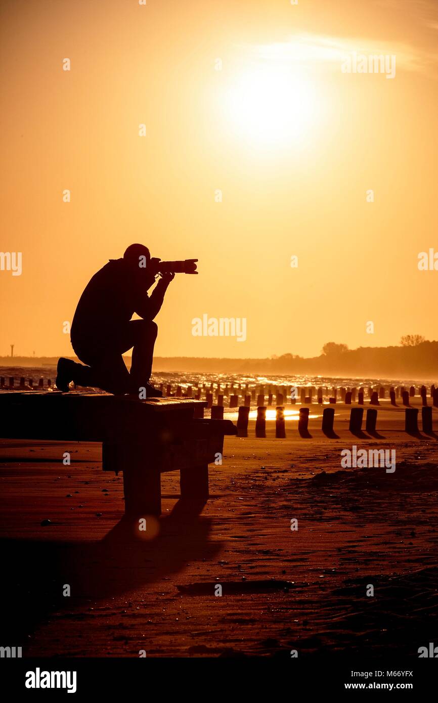 Silhouette de photographe agenouillée sur la plage dorée au cours de lever/coucher du soleil Banque D'Images