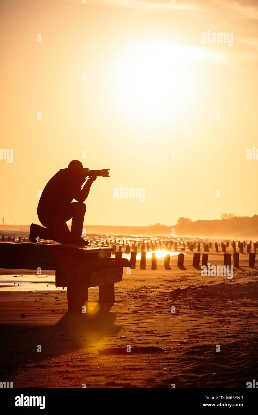 Silhouette de photographe agenouillée sur la plage dorée au cours de lever/coucher du soleil Banque D'Images