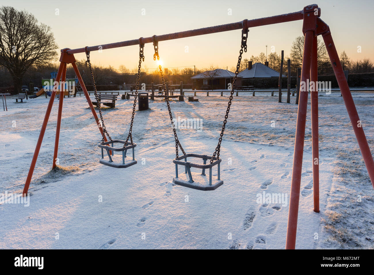 Balançoires dans une aire de jeux pour enfants au lever du soleil sur un jour d'hiver enneigé, Fordingbridge, New Forest, Hampshire, Royaume-Uni Banque D'Images