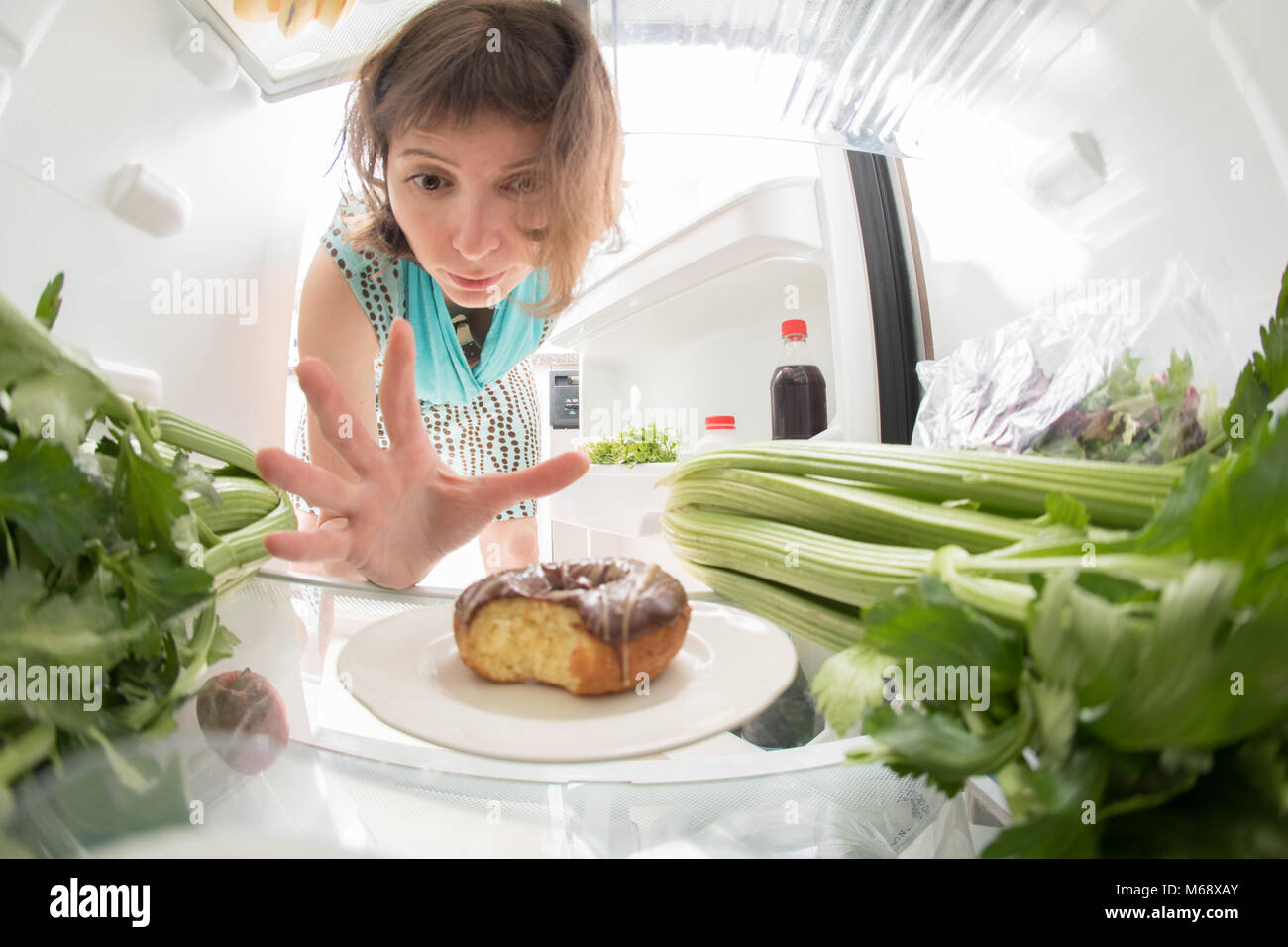 Lutte : régime alimentaire Une main saisissant un beigne de l'open réfrigérateur plein de verts. Banque D'Images